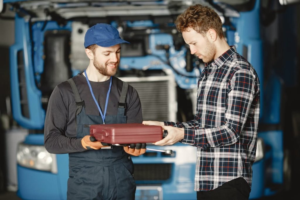 Two male mechanics discussing work in a garage workshop holding a toolbox.