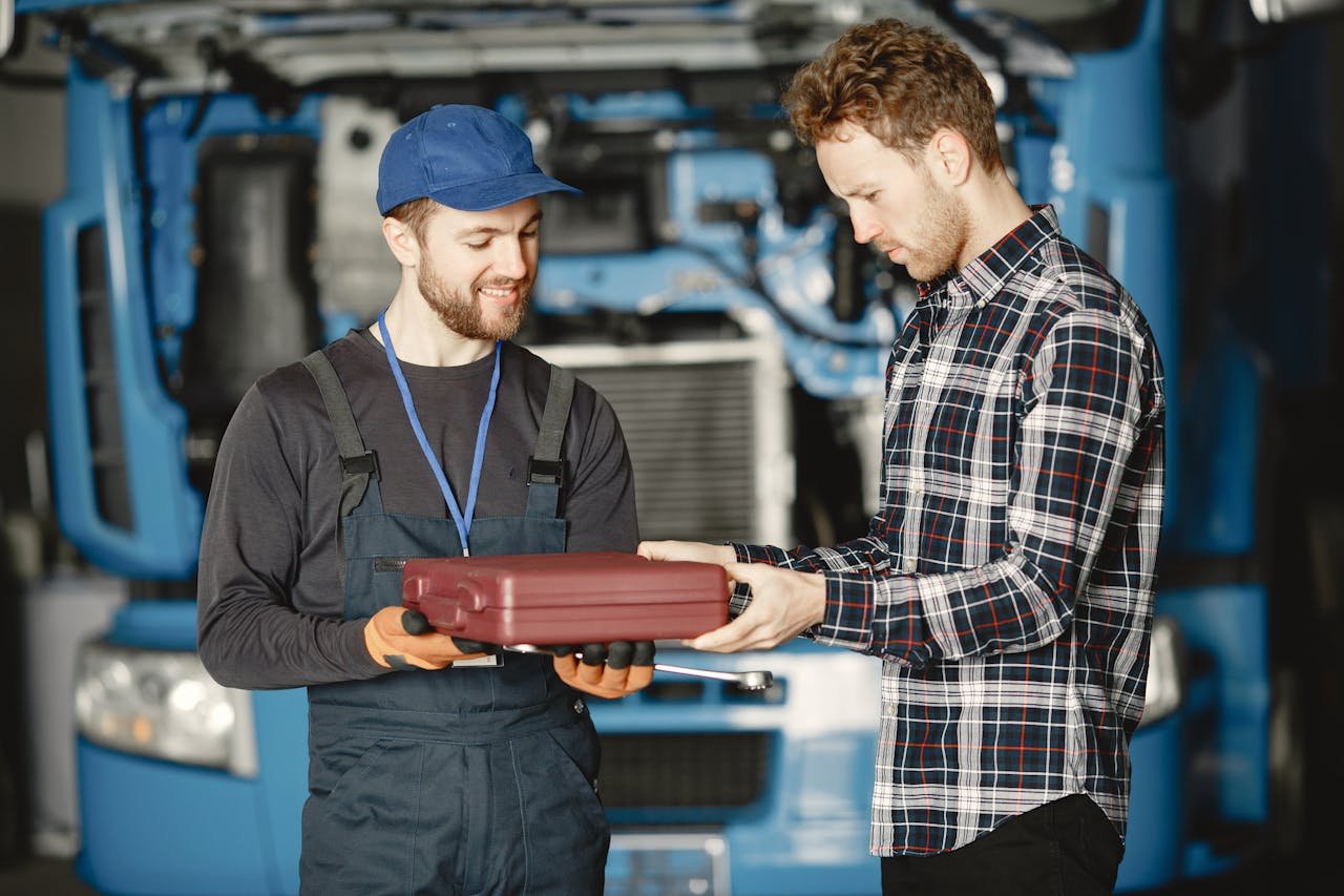creative-02 Two male mechanics discussing work in a garage workshop holding a toolbox.