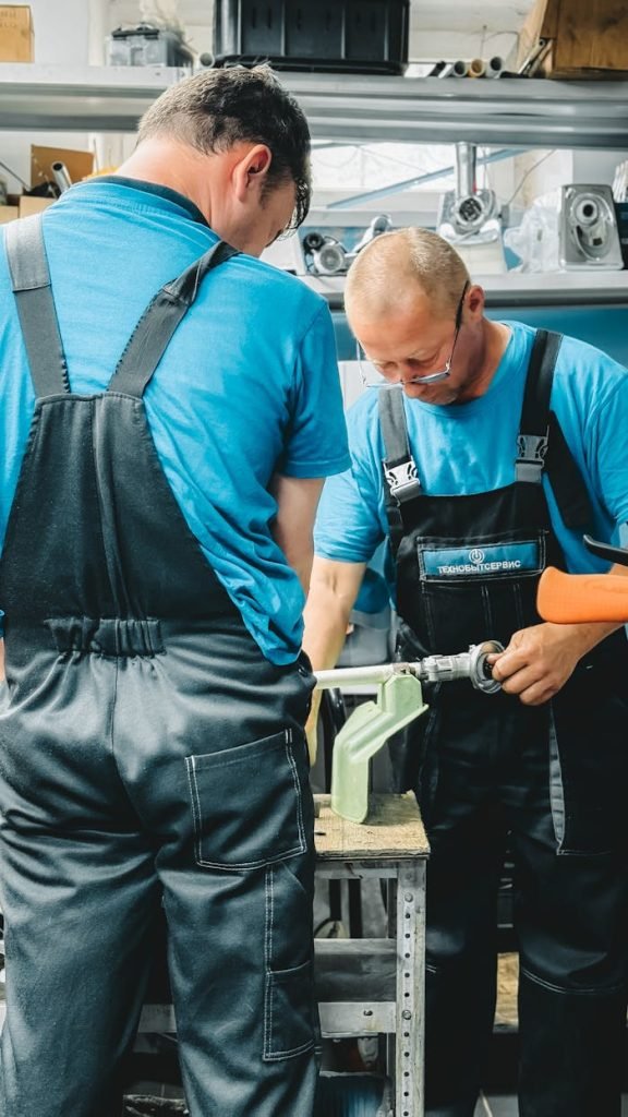Two male technicians work together using tools in a busy workshop.